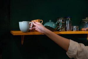 Donker flesgroene keukenmuur met een houten plank vol keramiek, theepot en voorraadpotten