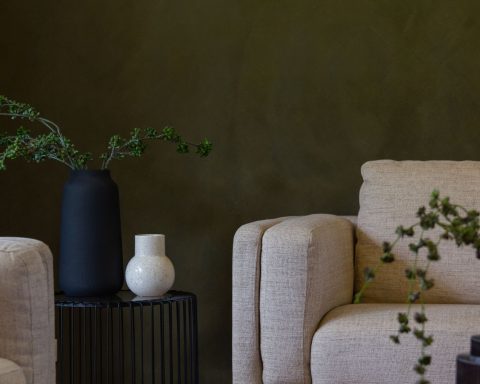 Minimalistische woonkamer met groene muren, twee stoelen, een tafeltje en planten in neutrale tinten