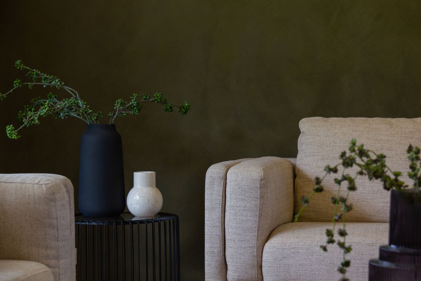 Minimalistische woonkamer met groene muren, twee stoelen, een tafeltje en planten in neutrale tinten