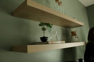 Groene muur met houten zwevende planken vol boeken, planten en karaffen in neutrale, natuurlijke tinten
