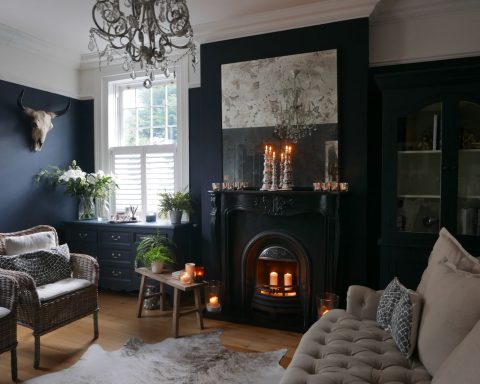 Klassieke woonkamer met donker stormblauwe muren, open haard, rieten stoelen en een zachte bank