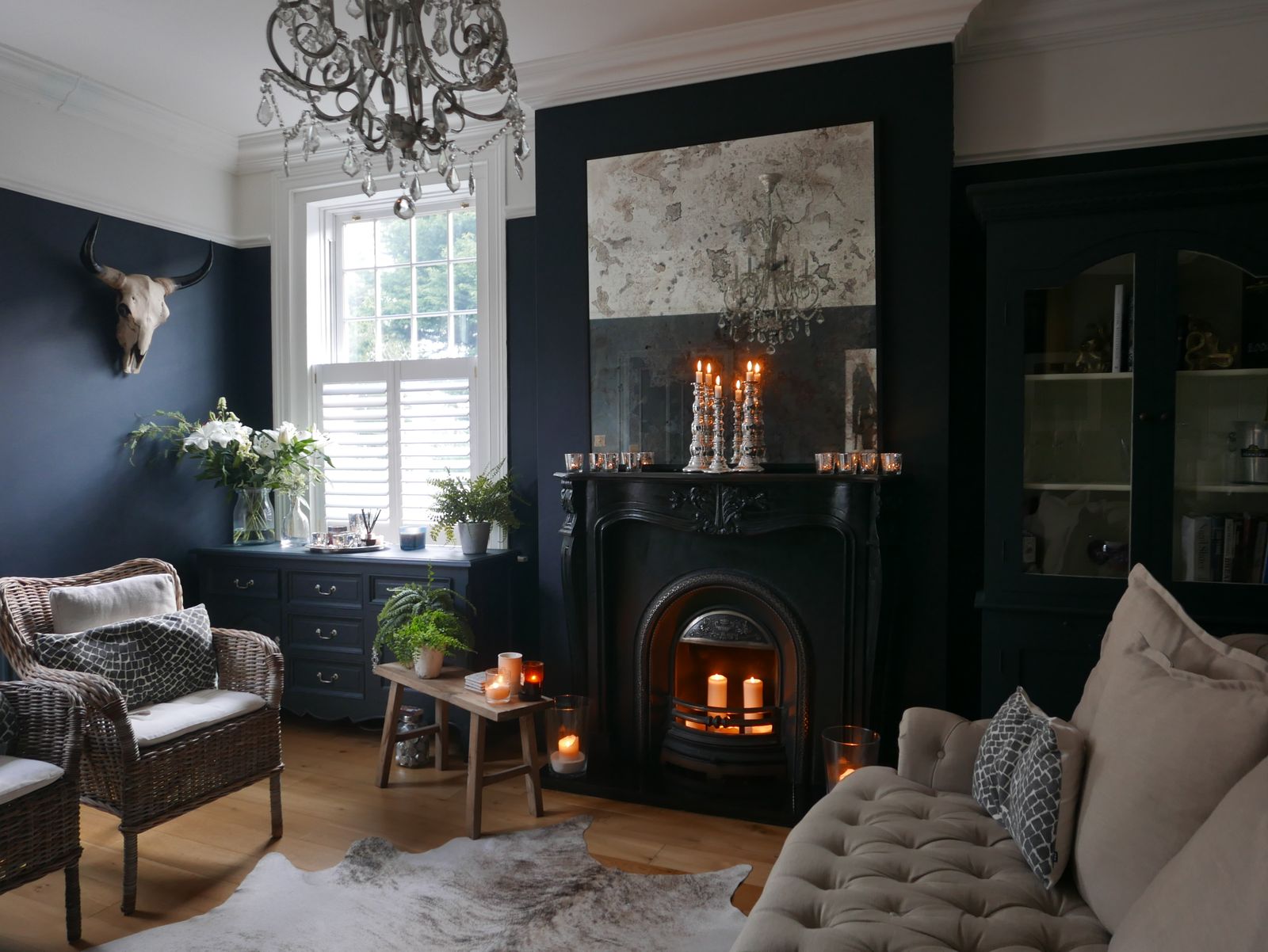 Klassieke woonkamer met donker stormblauwe muren, open haard, rieten stoelen en een zachte bank