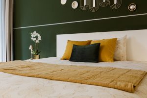 Slaapkamer met een donker olijfgroene muur, okergele kussens en een mosterdkleurige sprei