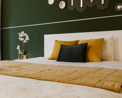 Slaapkamer met een donker olijfgroene muur, okergele kussens en een mosterdkleurige sprei
