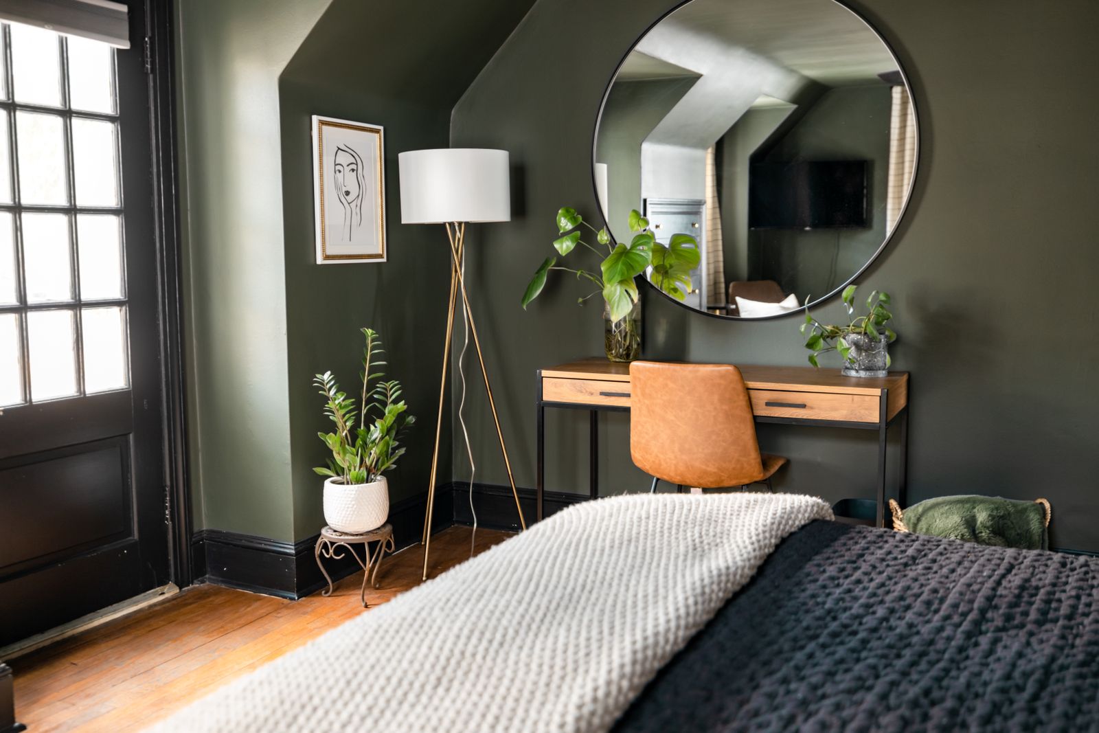 Slaapkamer met gedempt saliegroene muren, houten bureau, ronde spiegel en planten