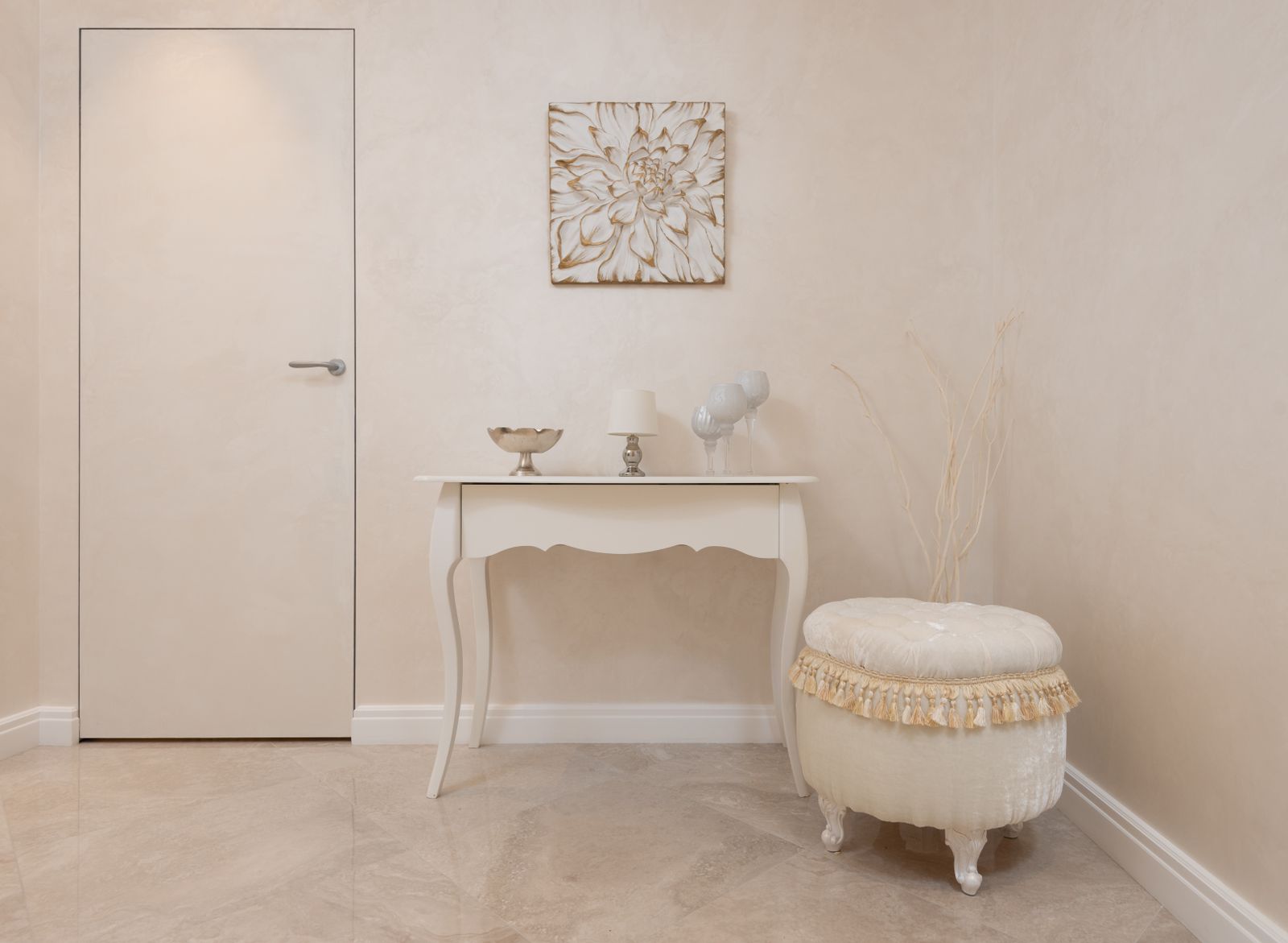 Lichte hal met beige muren, een beige tafel en een zachte poef in een rustig, neutraal interieur