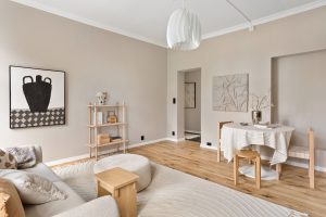 Lichte woonkamer met bleke greige muren, houten meubels, een witte hanglamp en een ronde eettafel
