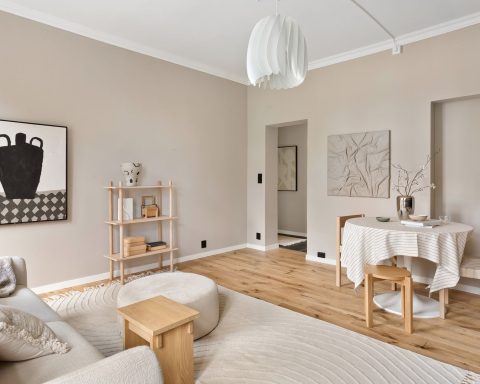 Lichte woonkamer met bleke greige muren, houten meubels, een witte hanglamp en een ronde eettafel