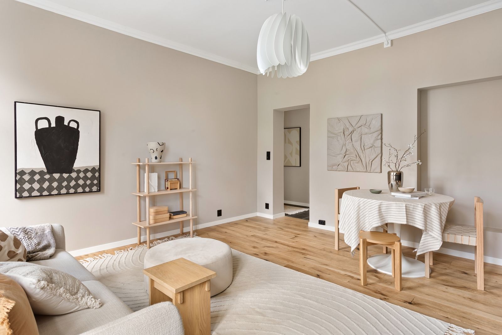 Lichte woonkamer met bleke greige muren, houten meubels, een witte hanglamp en een ronde eettafel